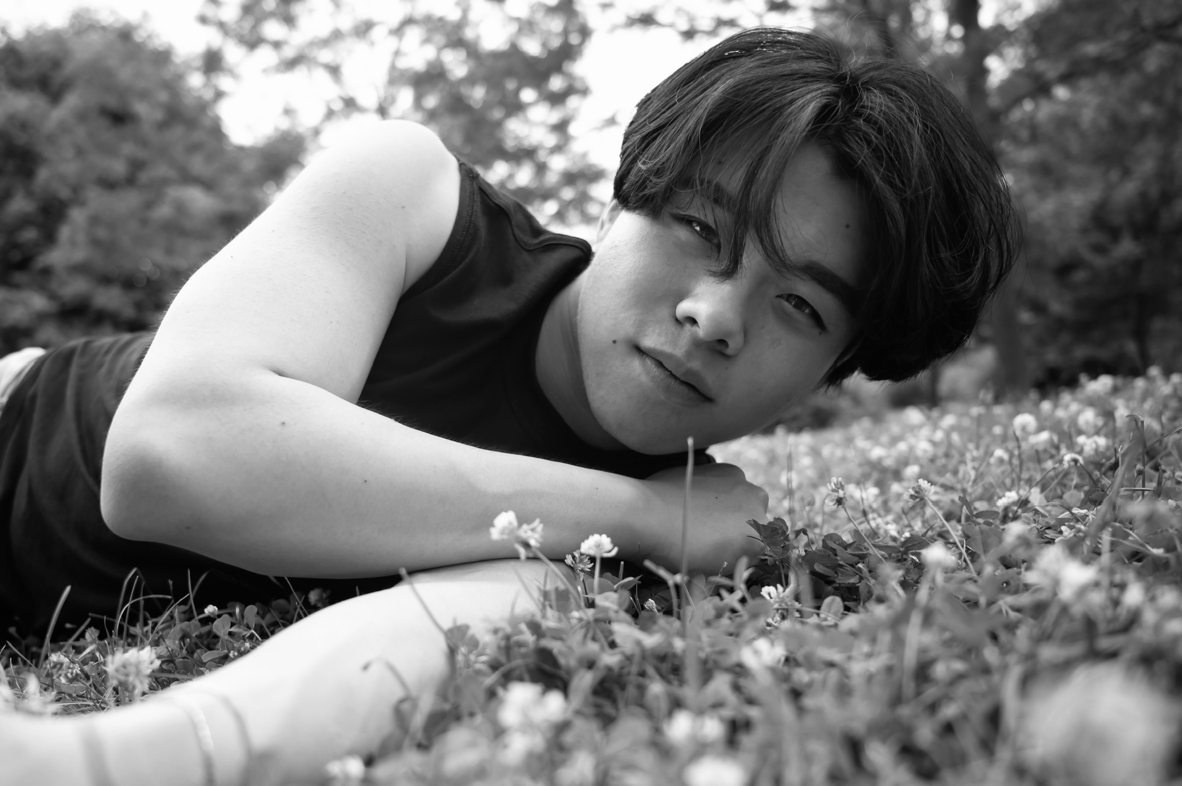 Jun Lucas lying in the grass, looking directly at the camera in a black-and-white portrait
